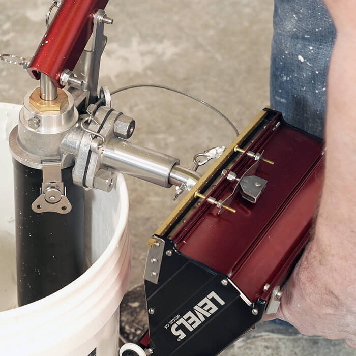 Person using Level 5 box filler attached to a compound pump to load mud from a bucket into a Level 5 flat box